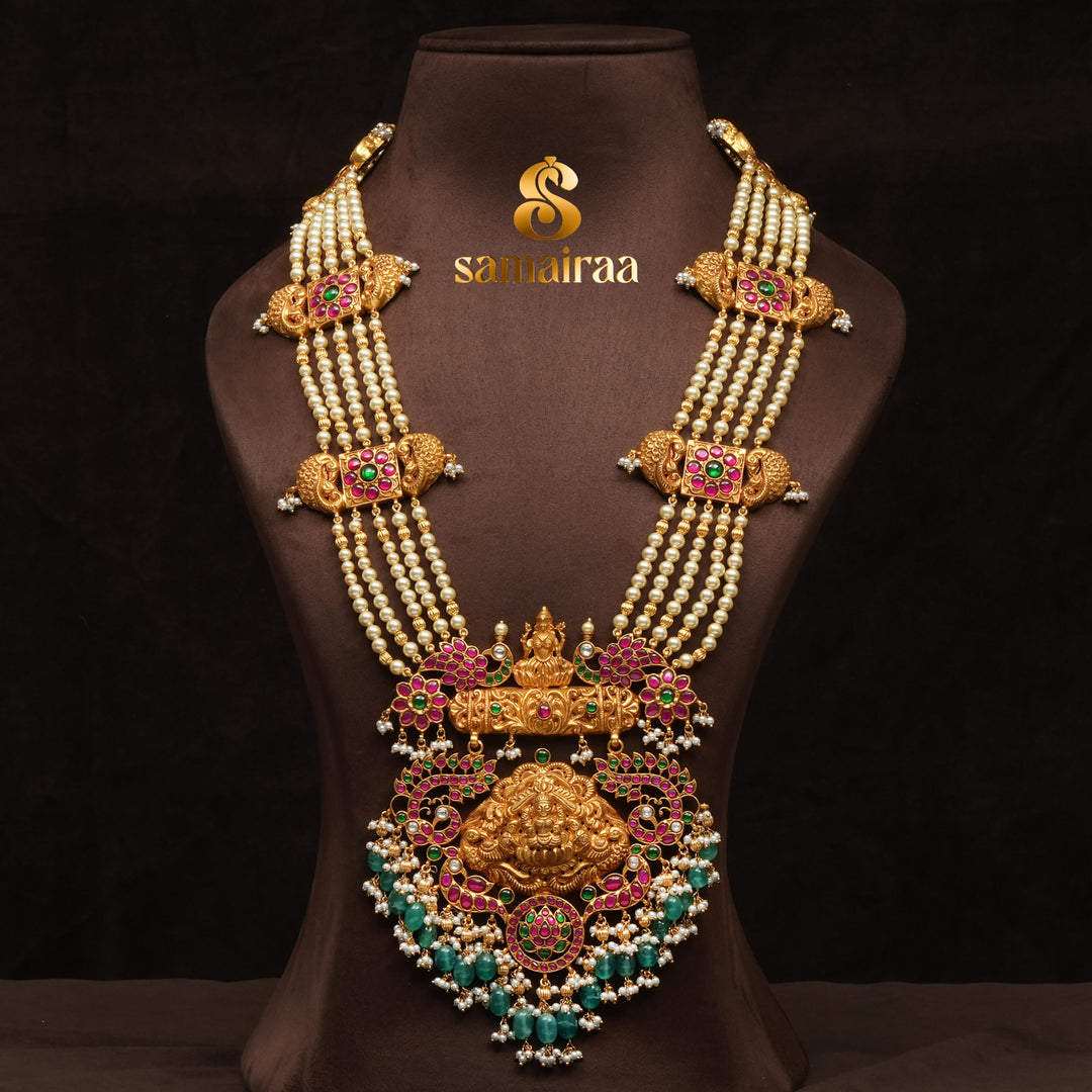 Traditional pearl haram necklace in 92.5 silver with antique gold finish, Lakshmi pendant, kundan stones and green bead drops for South Indian bridal jewellery by Sri Fine Jewellery Hyderabad.
