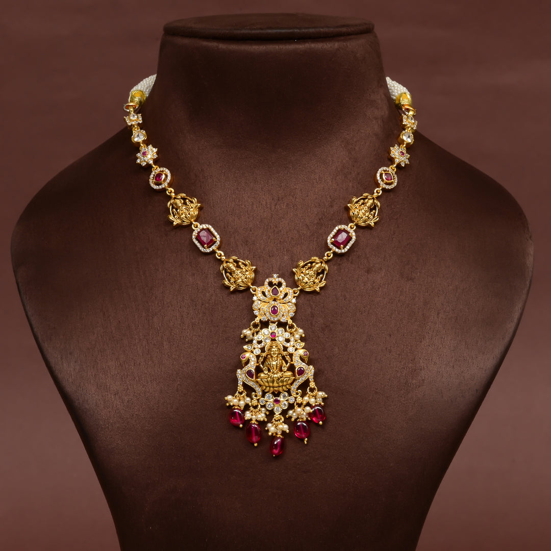 Elegant 92.5 silver temple necklace featuring intricate Lakshmi motif craftsmanship with ruby-toned stones, pearl detailing, and traditional antique gold finish. Handcrafted designer necklace with premium cz embellishments, perfect for bridal wear, festive occasions, weddings, and traditional ethnic styling.
Sri Fine Jewellery, Hyderabad 