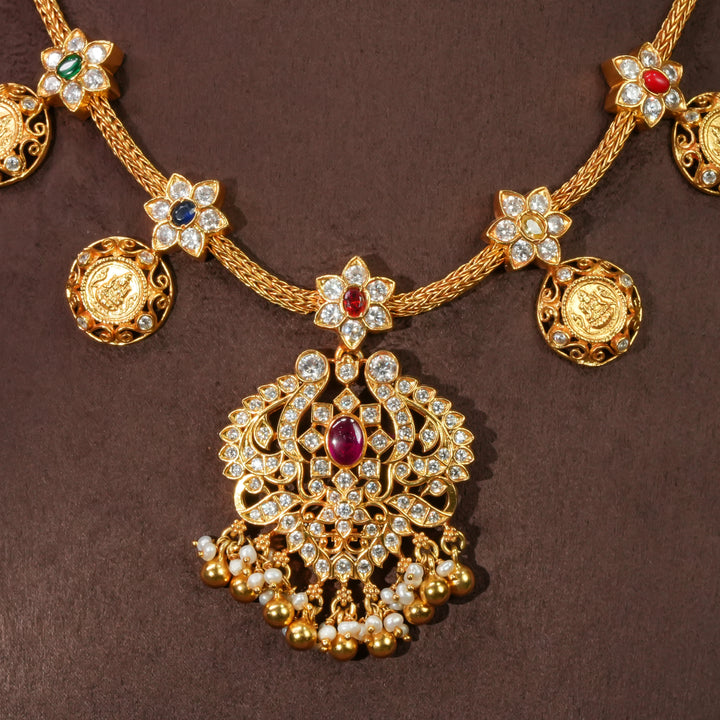Close-up view of 92.5 sterling silver floral necklace with antique coin motifs, ruby stone centerpiece, cz detailing, and traditional South Indian bridal pendant in premium gold finish by Sri Fine Jewellery Hyderabad.
(https://srifinejewellery.com)