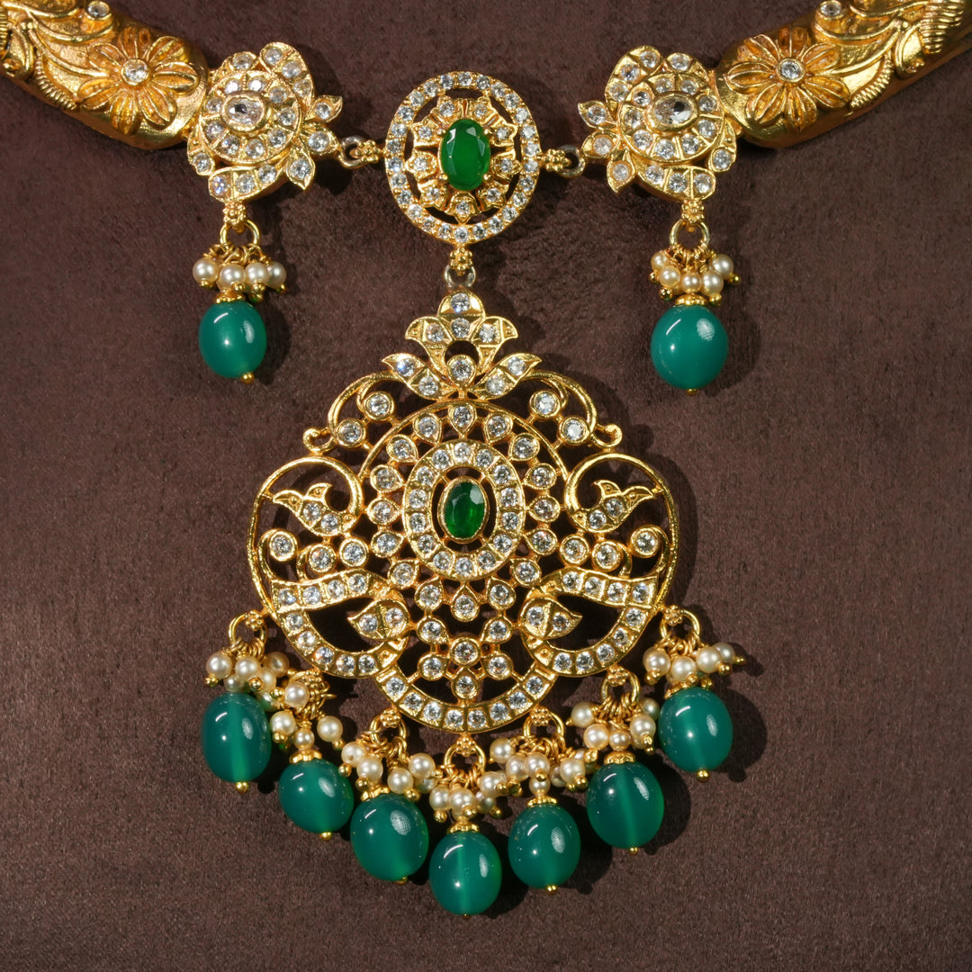 Close-up view of 92.5 sterling silver antique necklace with emerald green stone drops, intricate floral detailing, temple-inspired craftsmanship, and gold-finish elegance by Sri Fine Jewellery Hyderabad.
